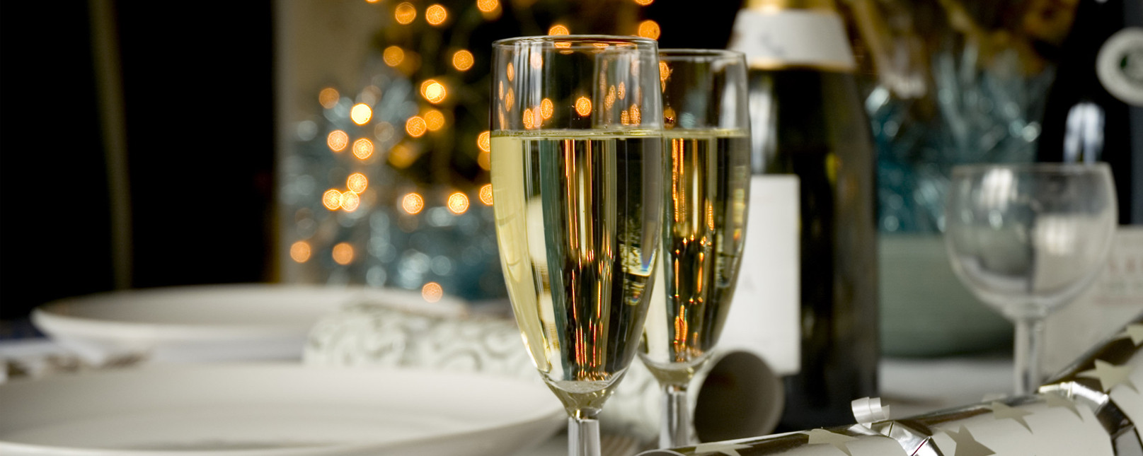 Two champagne glasses sitting one a white table with a champagne bottle and some plates and cutlery within the backdrop